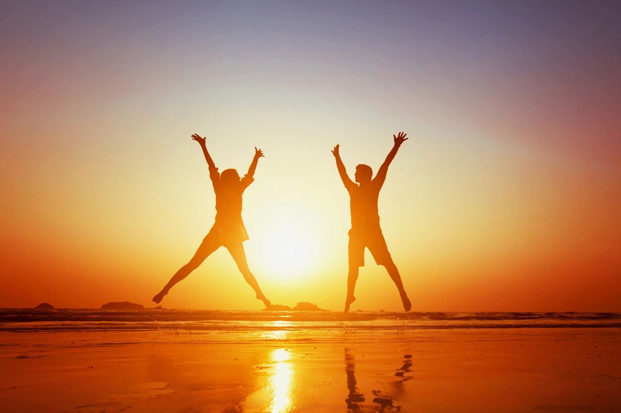 Two people jumping in the air on a beach.